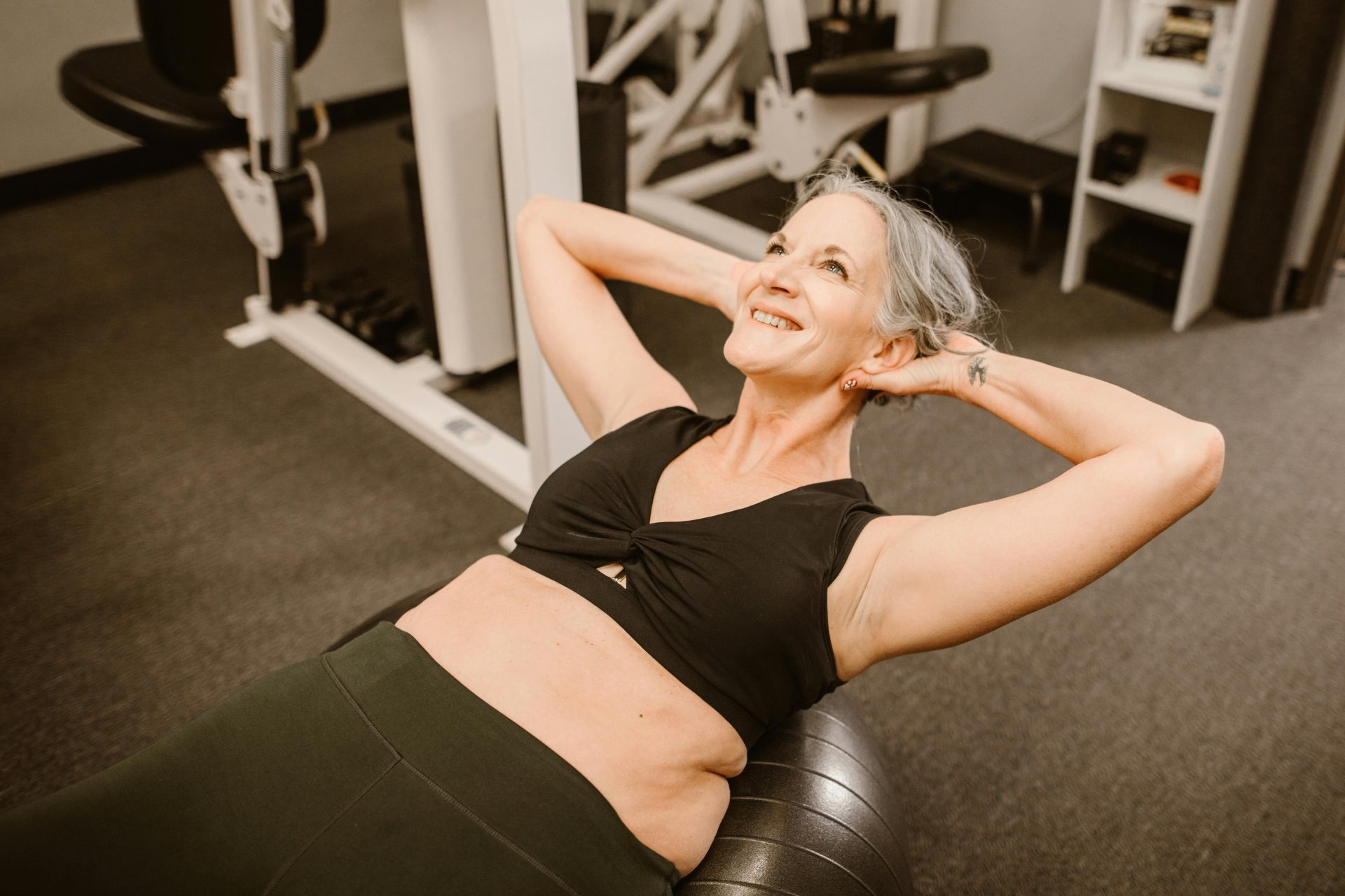 Eine ältere Frau mit grauem Haar lächelt, während sie in einem Fitnessstudio mit einem Medizinball trainiert.