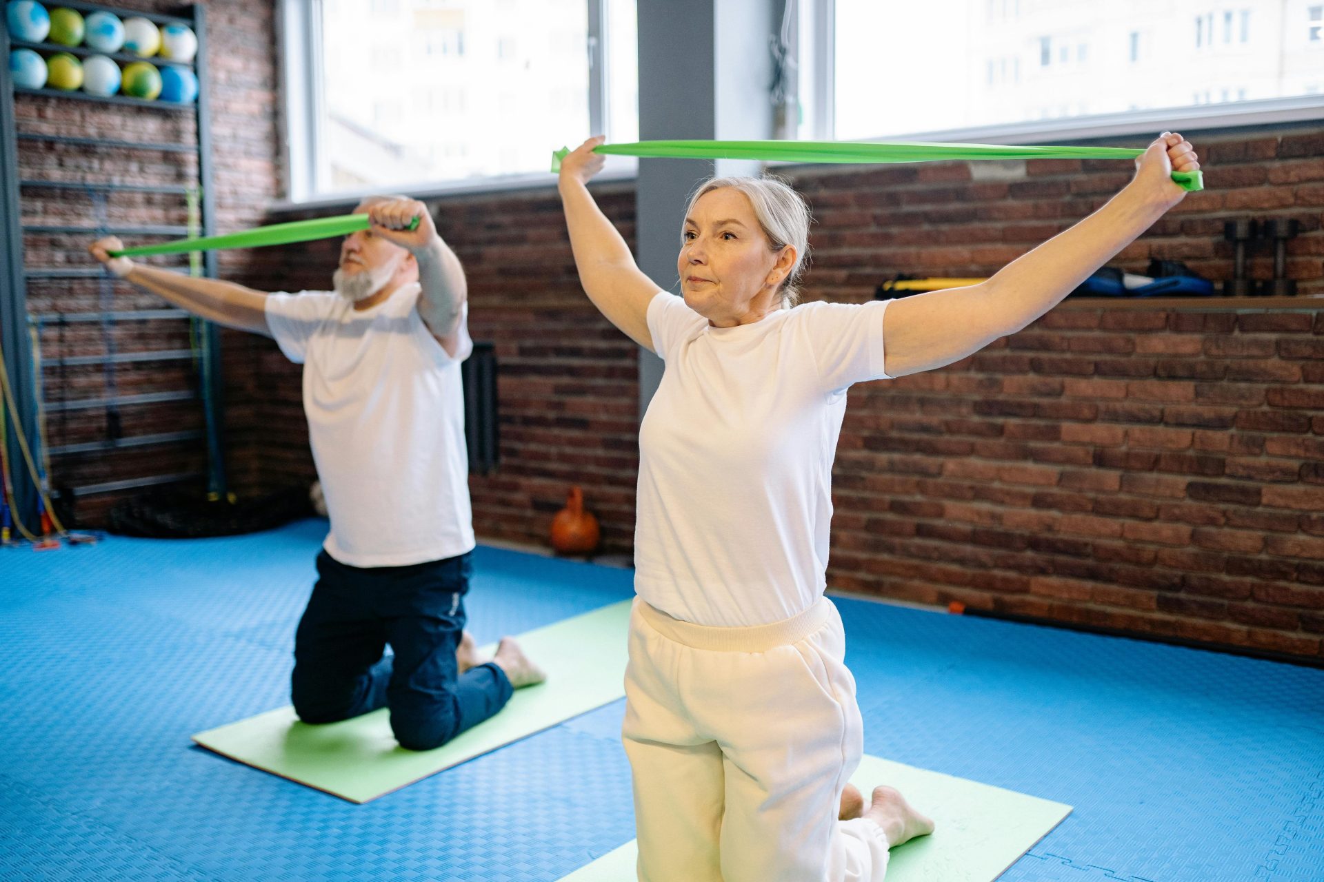 Ein älterer Mann und eine ältere Frau absolvieren ein Fitnesstraining mit Widerstandsbändern und fördern so einen gesunden Lebensstil in Innenräumen.