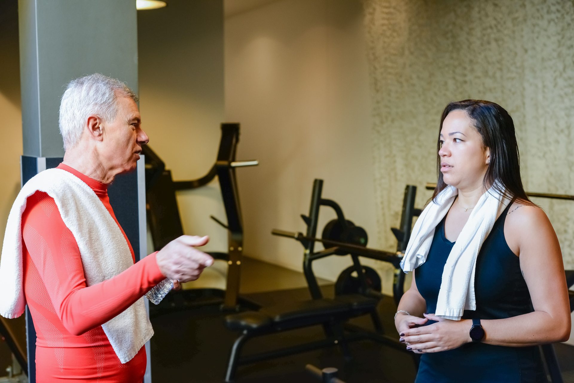 Ein älterer Mann und eine ältere Frau unterhalten sich in einem Fitnessstudio über Fitnessroutinen.