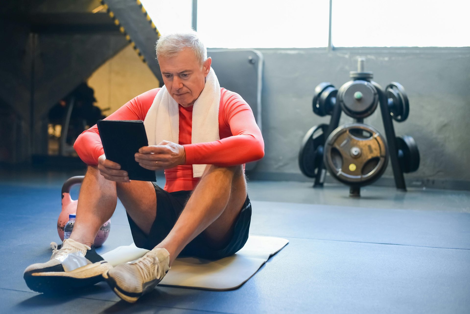 Ein älterer Mann in Sportkleidung überprüft während einer Trainingspause im Fitnessstudio sein Tablet.