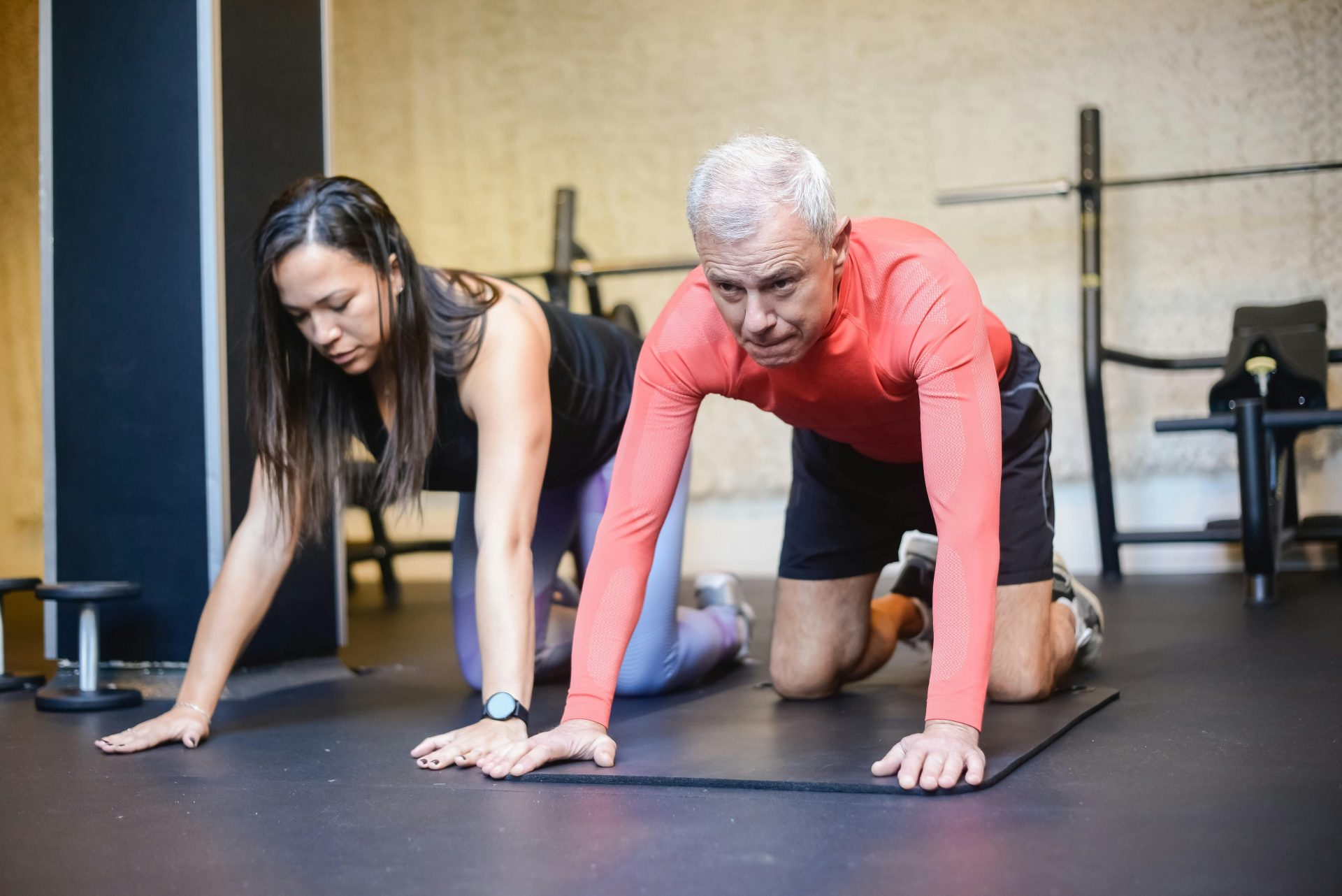 Ein älterer Mann und eine Trainerin führen in Innenräumen Fitnessübungen durch und fördern so gesundes Altern.