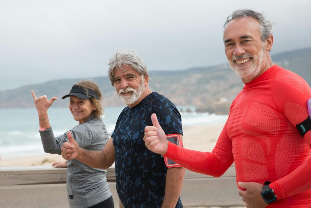 Lächelnde ältere Freunde beim Sport am Strand in Portugal, die einen gesunden Lebensstil pflegen.