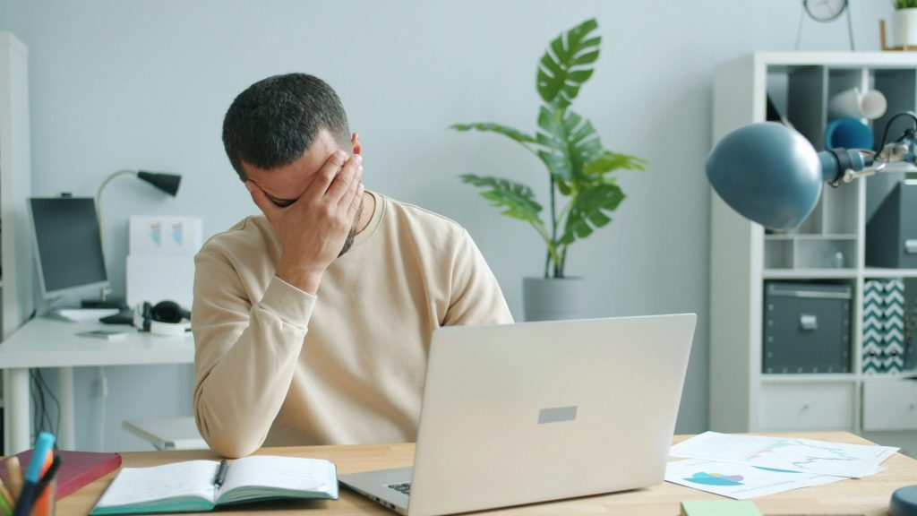 Man rubbing his face in front of laptop.